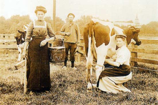 Met op de achtergrond de kerk van Oosterblokker poseren een boer en twee boerinnen omstreeks 1910 voor de fotograaf.