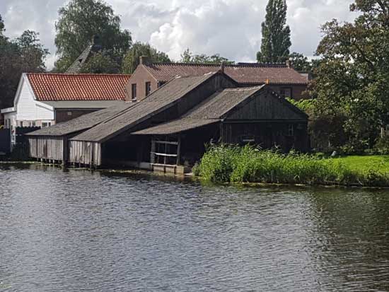 De schuitenhokken aan het water met de twee lagere schuren en de hoge stenen schuur daarachter.