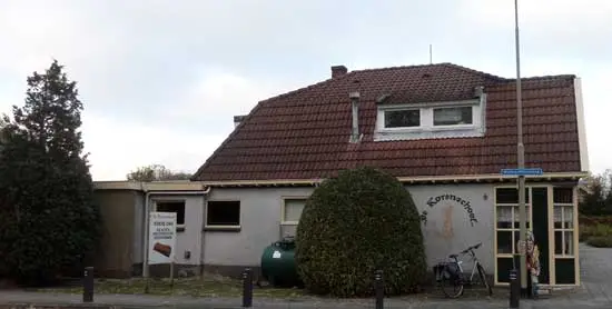 De olietank staat anno 2021 nog steeds tegen de zijgevel, enigszins verscholen achter een struik.