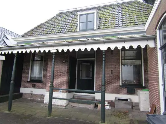 Overzicht van de achterzijde van het huis met de veranda of overkapping en rechts het kelderraam en de waterbak.
