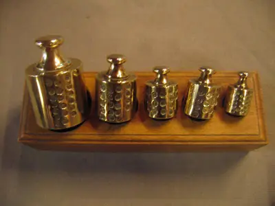 Een houten blokje met koperen gewichten voorzien van vele ijkmerken.
