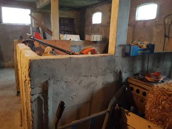 Binnenkant van de schuur met betonnen muur en raampjes.