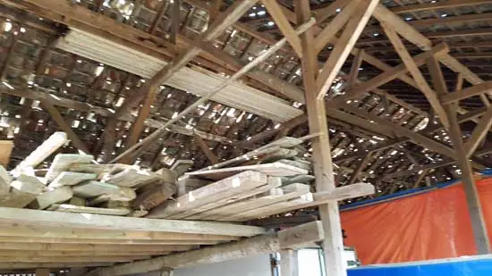 Houtopslag in de loods, duidelijk zijn de kieren in het dak te zien.